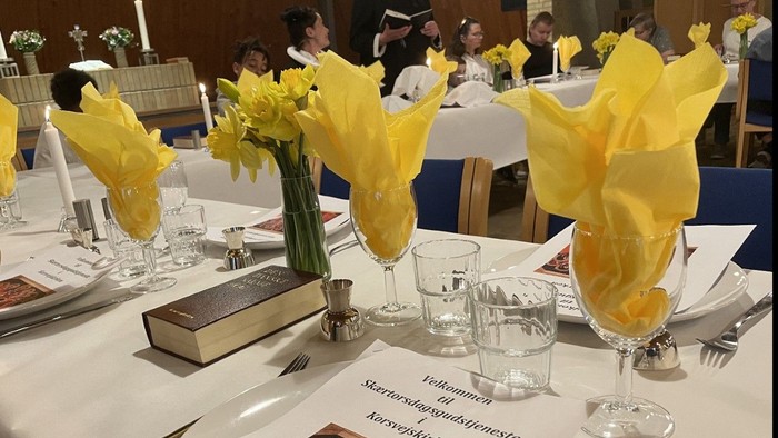 Bord er stillet med gule blomster og glas, mens folk sidder og snakker.