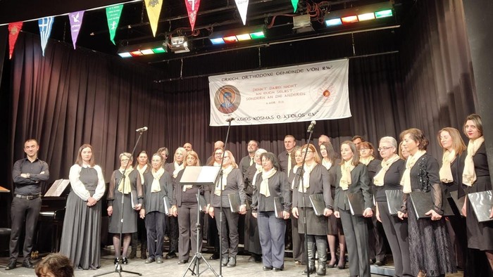 Un chœur se produit sur scène avec des drapeaux triangulaires colorés et une bannière en arrière-plan.