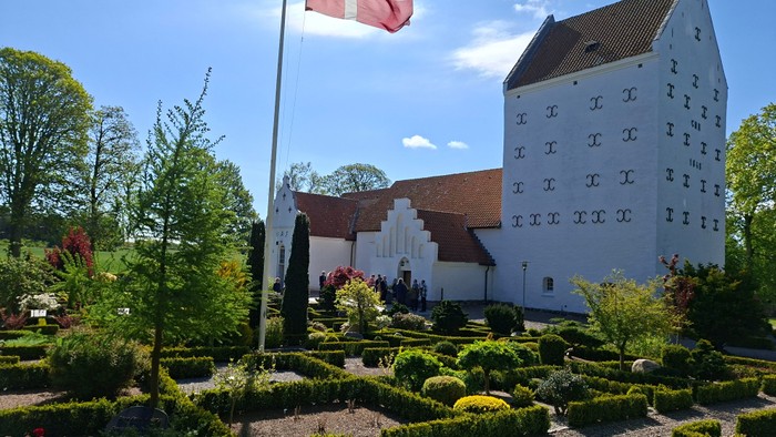 Dansk flag på kirkegård med hvidt tårn og grønne planter