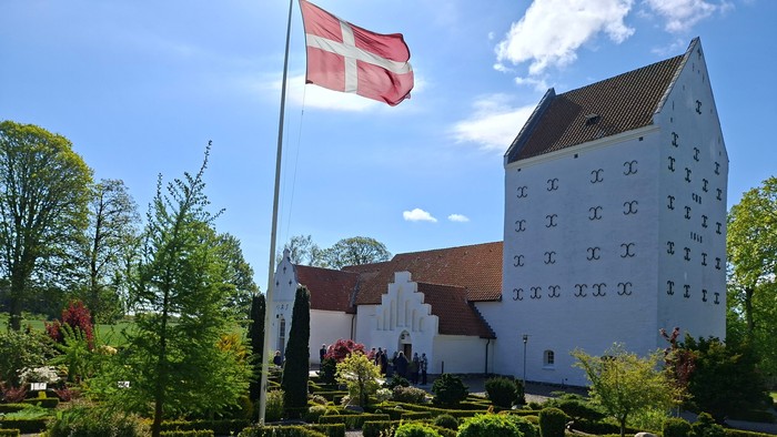 Dansk flag på kirkegård med hvidt tårn og grønne planter
