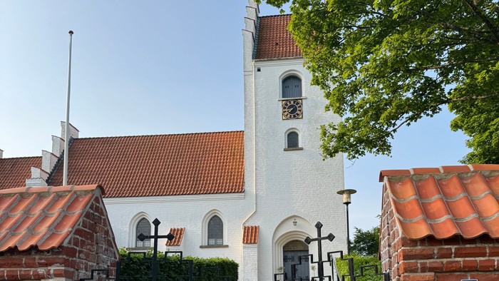 En hvid kirke med røde tag og mursten, med en sort gæld og træer ved siden af