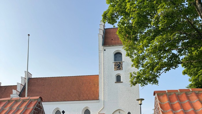 En hvid kirke med røde tag og mursten, med en sort gæld og træer ved siden af
