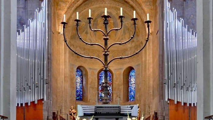 Ein Kircheninneres mit einem großen, verzierten Leuchter und farbenfrohen Buntglasfenstern.