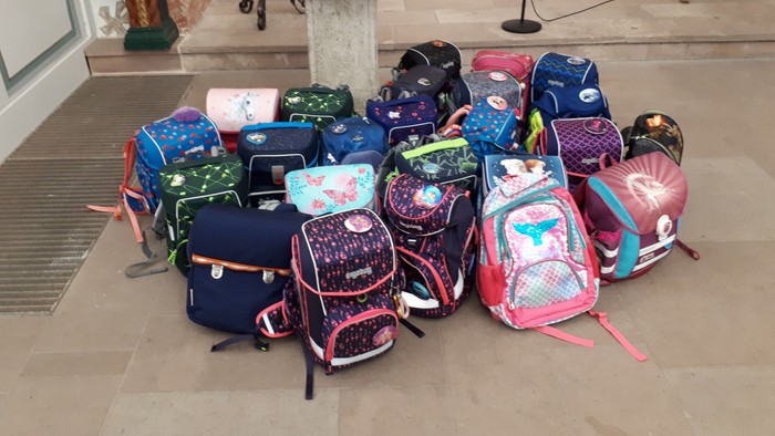 Rucksäcke in verschiedenen Farben und Mustern sind auf einem Steinboden übereinander gestapelt.