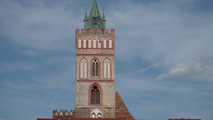 Turm einer historischen Backsteinkirche mit spitzem grünen Dach und gotischen Fenstern