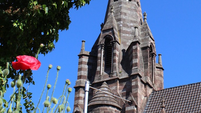 Der Kirchturm erhebt sich über bunte Blumen und einen grünen Baum.