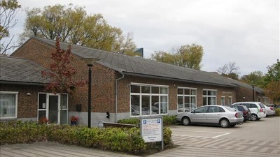 En lav, længgende bygning med røde mursten og store vinduer, med flere biler parkeret foran