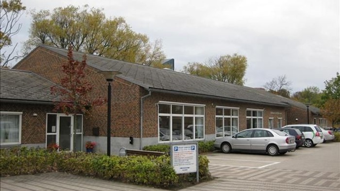 En lav, længgende bygning med røde mursten og store vinduer, med flere biler parkeret foran