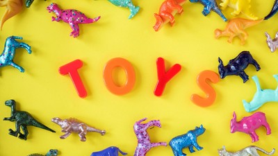 Colorful toy dinosaurs and letters spelling "TOYS" on yellow background