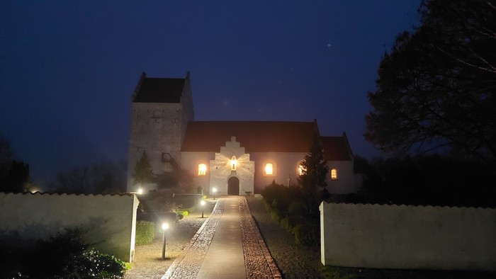 En belyst kirke med tårn og murvej til indgangen