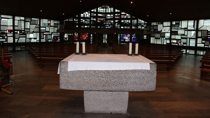 Ein moderner Altar in einer großen, dunklen Kirche mit vielen Fenstern.