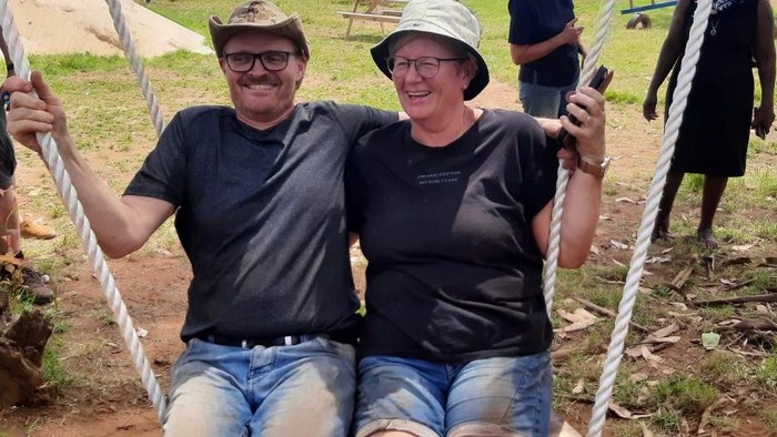 Foto af Bente og Peter Madsen på en stor gynge på en afrikansk legeplads. De er lidt beskidte af den røde jord.