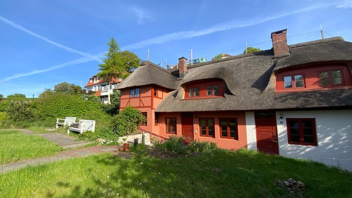 Das Bild zeigt ein charmantes, rotes Haus mit Strohdach in ländlicher Umgebung.