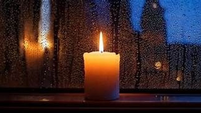 En lysende lyse stånder ved et regnede vindue med udsigt til en mørk skov.