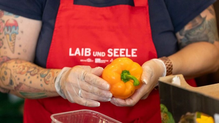 Person hält eine gelbe Paprika, trägt eine rote Schürze und Handschuhe.