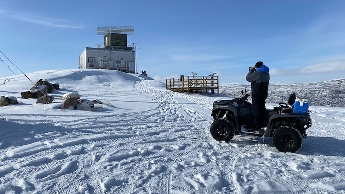 To dyr på ATV'er i sneede landskab med en tårnagtig bygning i baggrunden