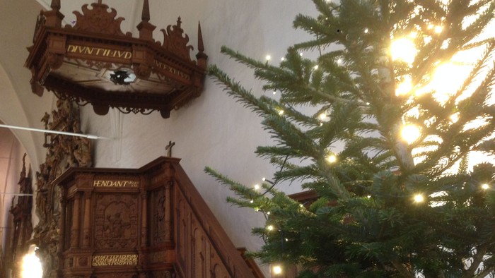 En juletree med lys og en gammel klokke i kirke