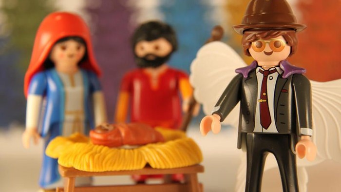 Drei Playmobil-Figuren stehen vor einem gelben Wagen, eine mit Hut und Krawatte.
