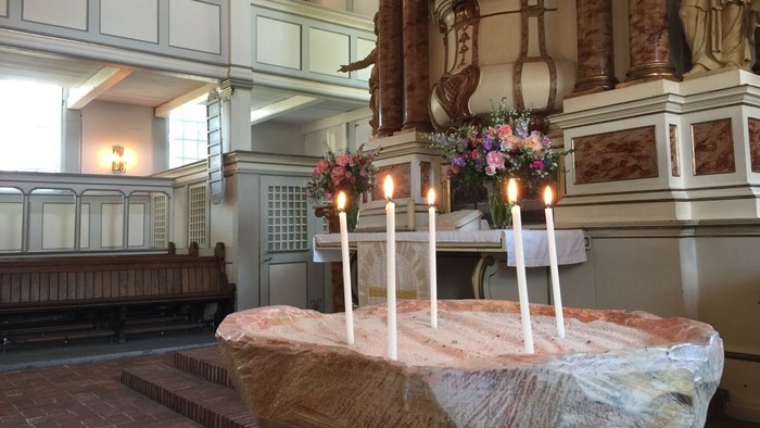 In der Kirche stehen drei brennende Kerzen auf einem Tisch mit Blumen.