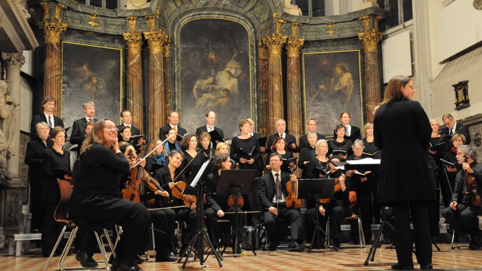 Ein Orchester spielt in einem prächtigen Saal mit großen Gemälden