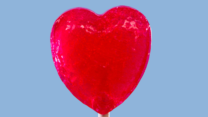 Ein glänzender, rot herzförmiger Luftballon vor blauem Hintergrund.