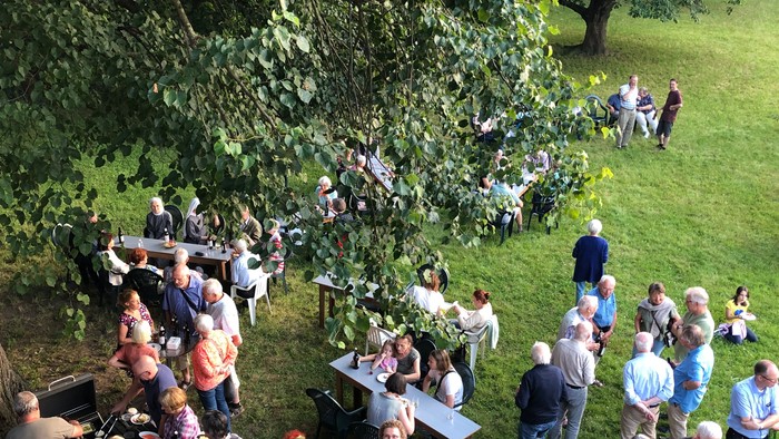 Eine große Gruppe von Menschen steht auf einem grasbewachsenen Bereich und unterhält sich.