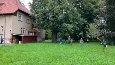 Kinder spielen auf einem großen, grünen Rasen vor einem Haus.
