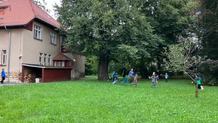 Kinder spielen auf einem großen, grünen Rasen vor einem Haus.