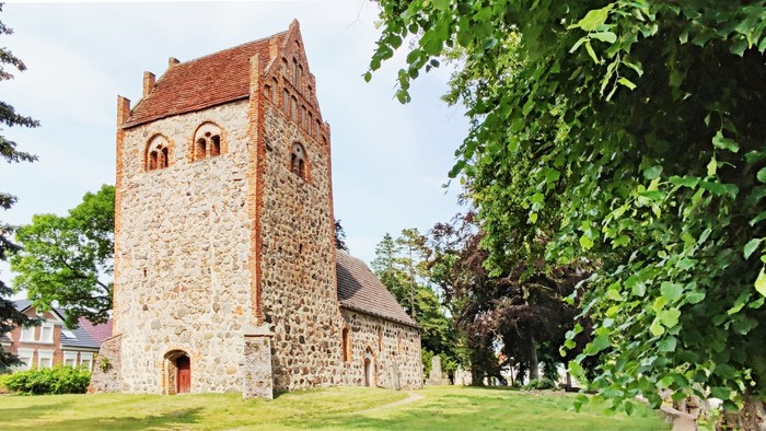 Alte Kirche mit Turm aus Stein, umgeben von Bäumen und Gras