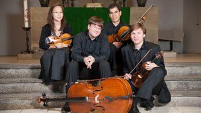 Ein Quartett von Musikerinnen und Musikern, die Streichinstrumente – Violine, Cello und Viola – spielen und sich formell gemeinsam präsentieren.