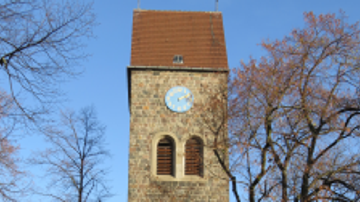 Alter Kirchturm mit Uhr und buntem Glasfenster, umgeben von Bäumen