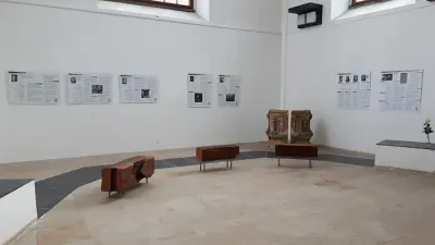 Ein großer Raum mit weißen Wänden und großen Fenstern, in dem mehrere Sessel und eine Couch stehen, umgeben von ausgehängten Plakaten