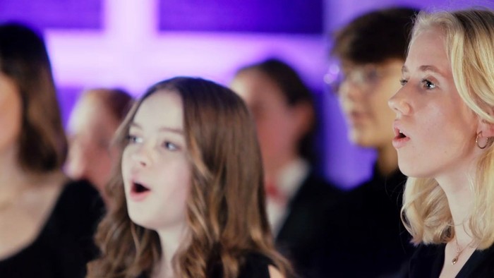 Eine Gruppe von Menschen, die leidenschaftlich auf der Bühne unter violettem Licht singt.