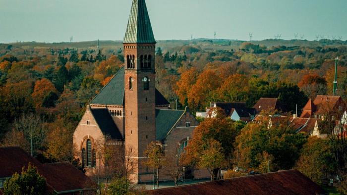 En kirke med høj tårn i et småby med høstfarvede træer