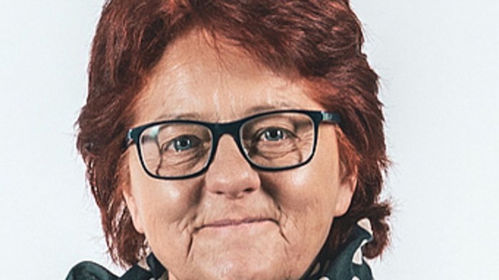 En kvinde med rødt hår og briller, der bærer en grøn skjorte med hvide prikker og en grøn skærm med hvide prikker.