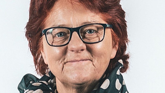 En kvinde med rødt hår og briller, der bærer en grøn skjorte med hvide prikker og en grøn skærm med hvide prikker.
