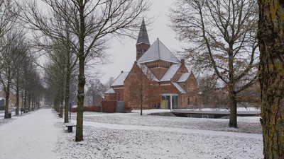 En snedækket park med en mørk teglsteinskirke med spisse tårn.