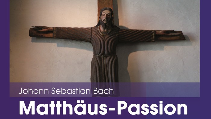 Ein hölzernes Kruzifix, das Jesus darstellt, mit einem darunter angebrachten Text, der auf Johann Sebastian Bachs „Matthäus-Passion“ verweist.