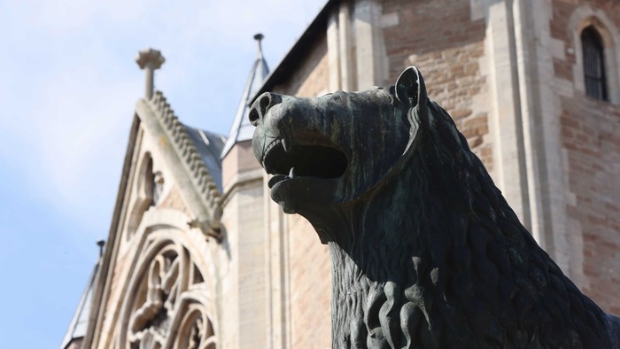 Eine bronzene Löwenstatue vor einem Gebäude im gotischen Stil.