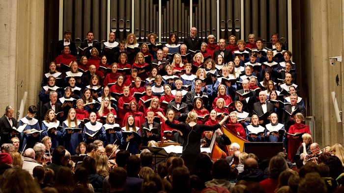Ein großer Chor singt in einer Kirche, dirigiert von einem Mann mit Stab.