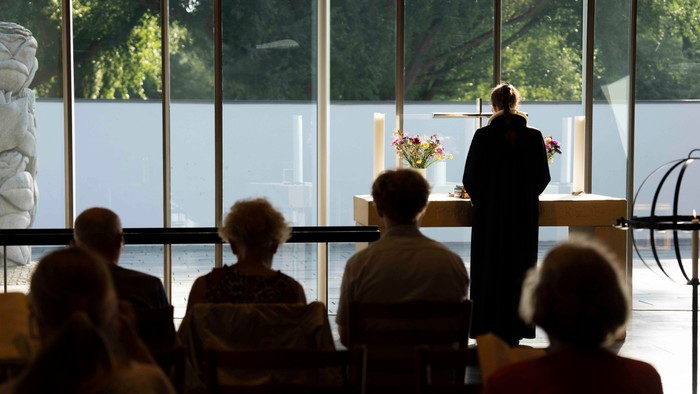 En præst holder et tale i en lys kirke med en gruppe tilhørere.