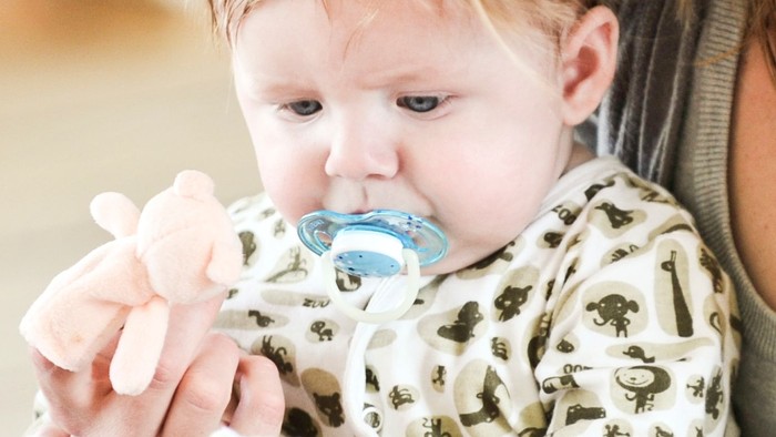 Et barn spiser fra en blå flaske, holdt af en voksende.