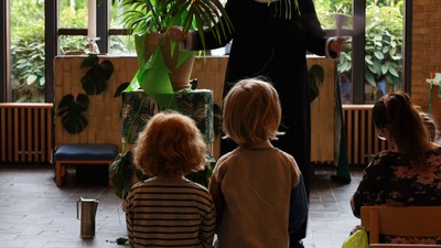 En kvinde og to børn ser på en grøn plante i et rum med mange planter.