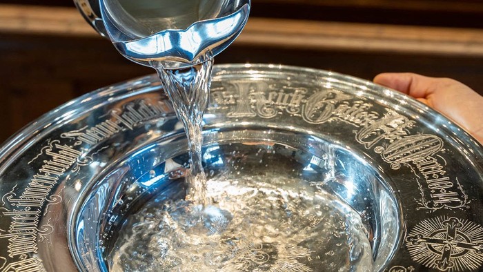 Hand gießt Wasser in silbernen Teller