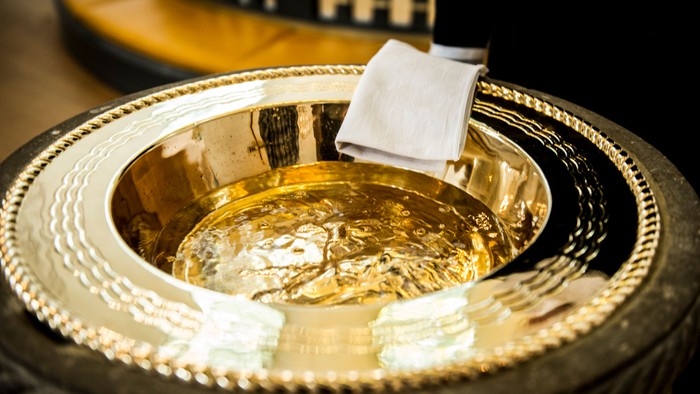 Gylden skål med klæde indeni, placeret på en udsmykket overflade.