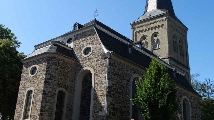 Das Bild zeigt eine steinerne Kirche mit hohem Turm und Rundbogenfenstern.