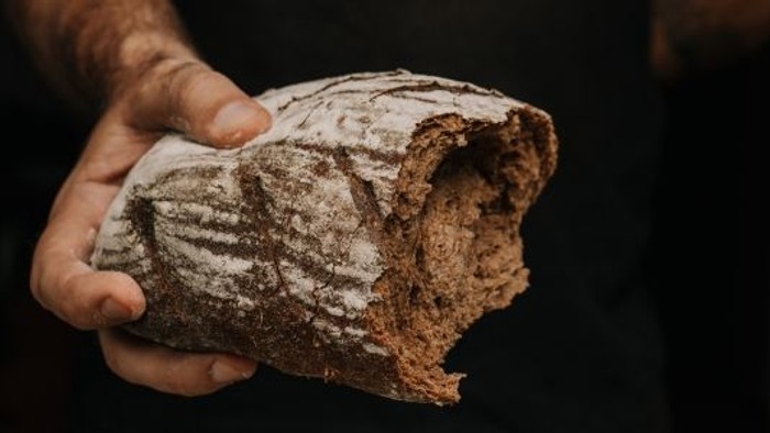 En hånd, der holder et rustikt, sprødt brød med synlige snitmærker, friskbagt.