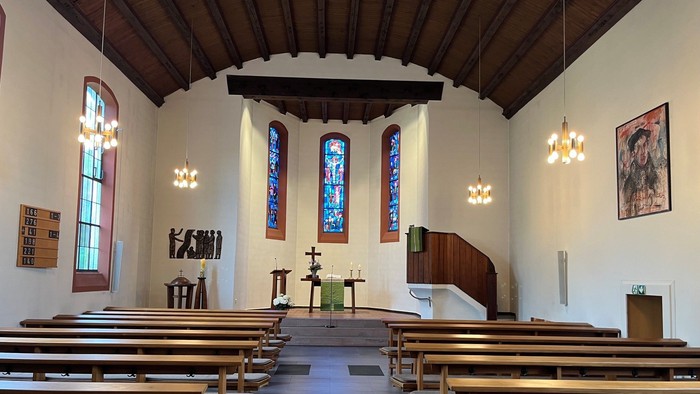 Moderne Kircheninnenausstattung mit hölzernen Kirchenbänken, Buntglasfenstern und minimalistischer Altarbeleuchtung.