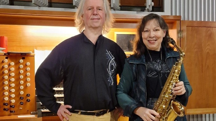 Ein Mann und eine Frau posieren mit einem Saxophon vor einem Orgelpfeifenregal.