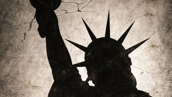 Silhuet af Frihedsgudinden, der holder en fakkel mod en revnet, forvitret baggrund.